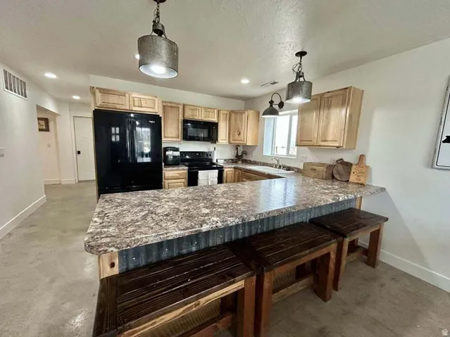 U-shaped kitchen with wood-finish cabinetry, black appliances, and a corrugated metal-clad breakfast bar