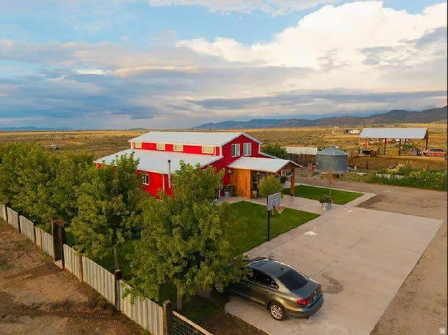 Red exterior with white trim, metal roof, concrete driveway, fenced perimeter, and established landscaping