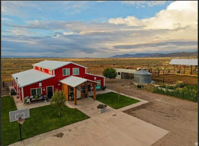 Red-sided exterior with a white roof, covered porch with wood columns, paved driveway, and established lawn