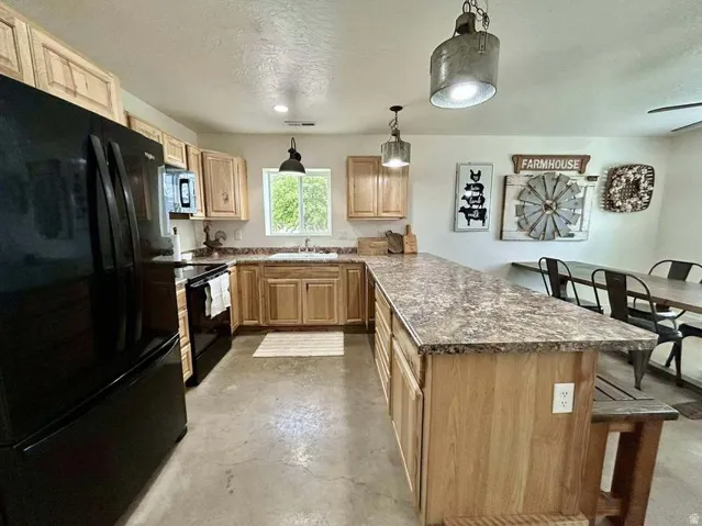 Kitchen featuring wood-finish cabinetry, black appliances, a double basin sink, and an extended countertop island