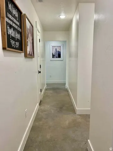 Recessed lighting illuminating a hallway with light-toned walls, white trim, and a concrete-finish floor
