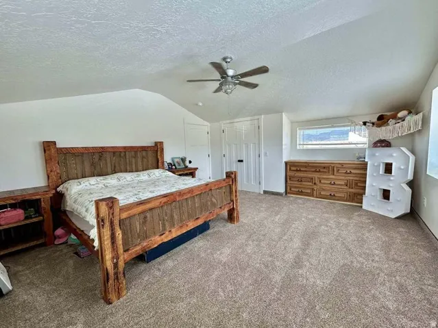 Vaulted ceiling with a ceiling fan, light-colored carpet flooring, white painted walls, and a horizontal window
