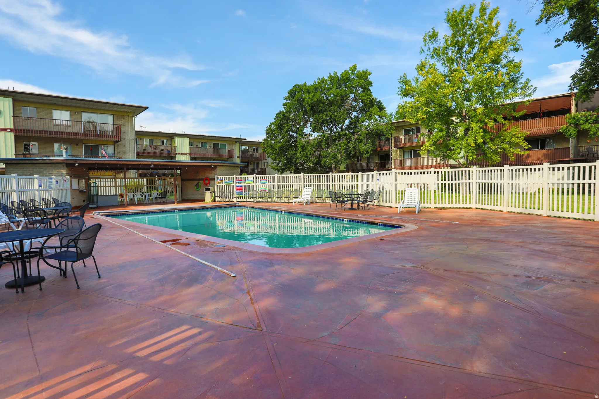 Communal swimming pool with a surrounding white picket fence and lounge area