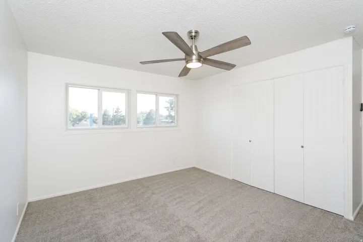 Grey carpet flooring, white walls, multiple windows, brushed nickel ceiling fan, and bi-fold closet doors