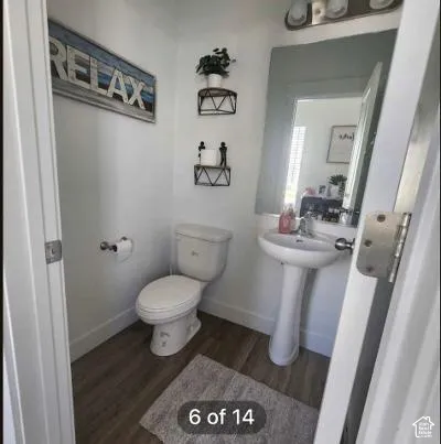 White pedestal sink, modern toilet, wood-finish flooring, and wall-mounted mirror
