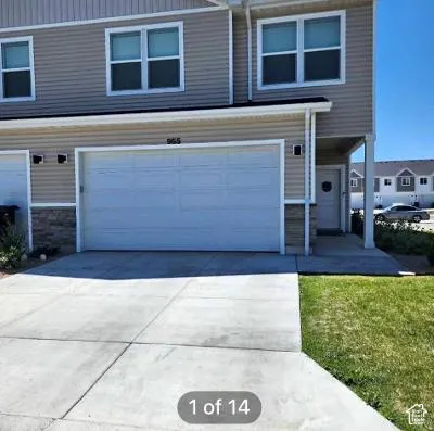 Light-toned siding exterior with stone accent, concrete driveway, attached garage, and covered entry