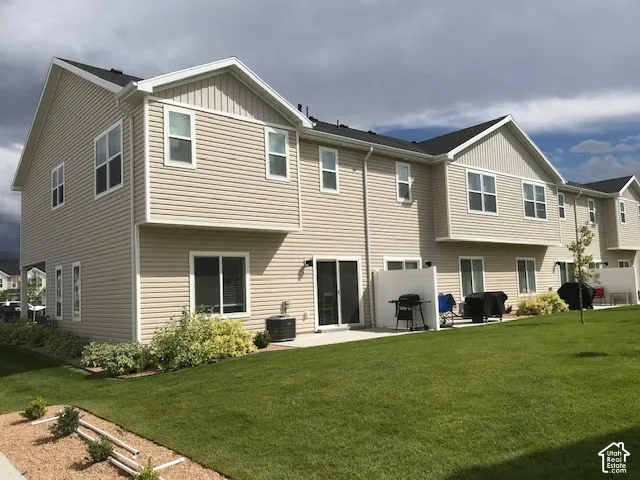 Rear exterior featuring a patio, sliding glass doors, multiple windows, and a landscaped yard