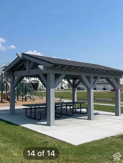 Covered outdoor pavilion featuring a dark shingle roof, painted structural wood, a concrete pad, and two picnic tables