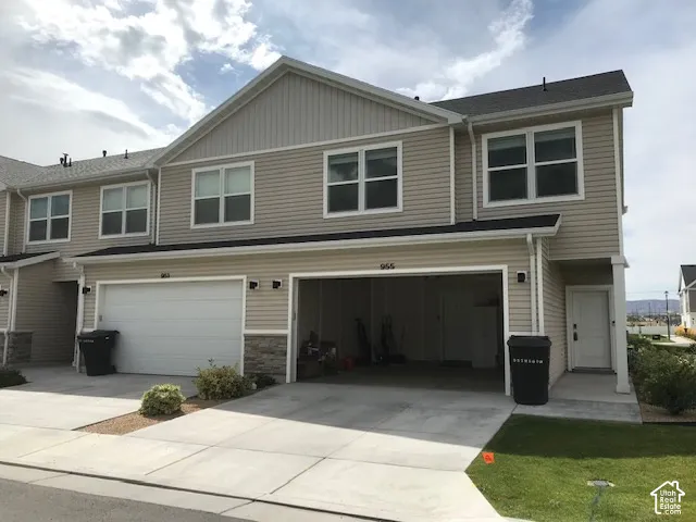 Contemporary townhouse exterior featuring light-colored siding, a dark shingle roof, white trim windows, and an integrated garage