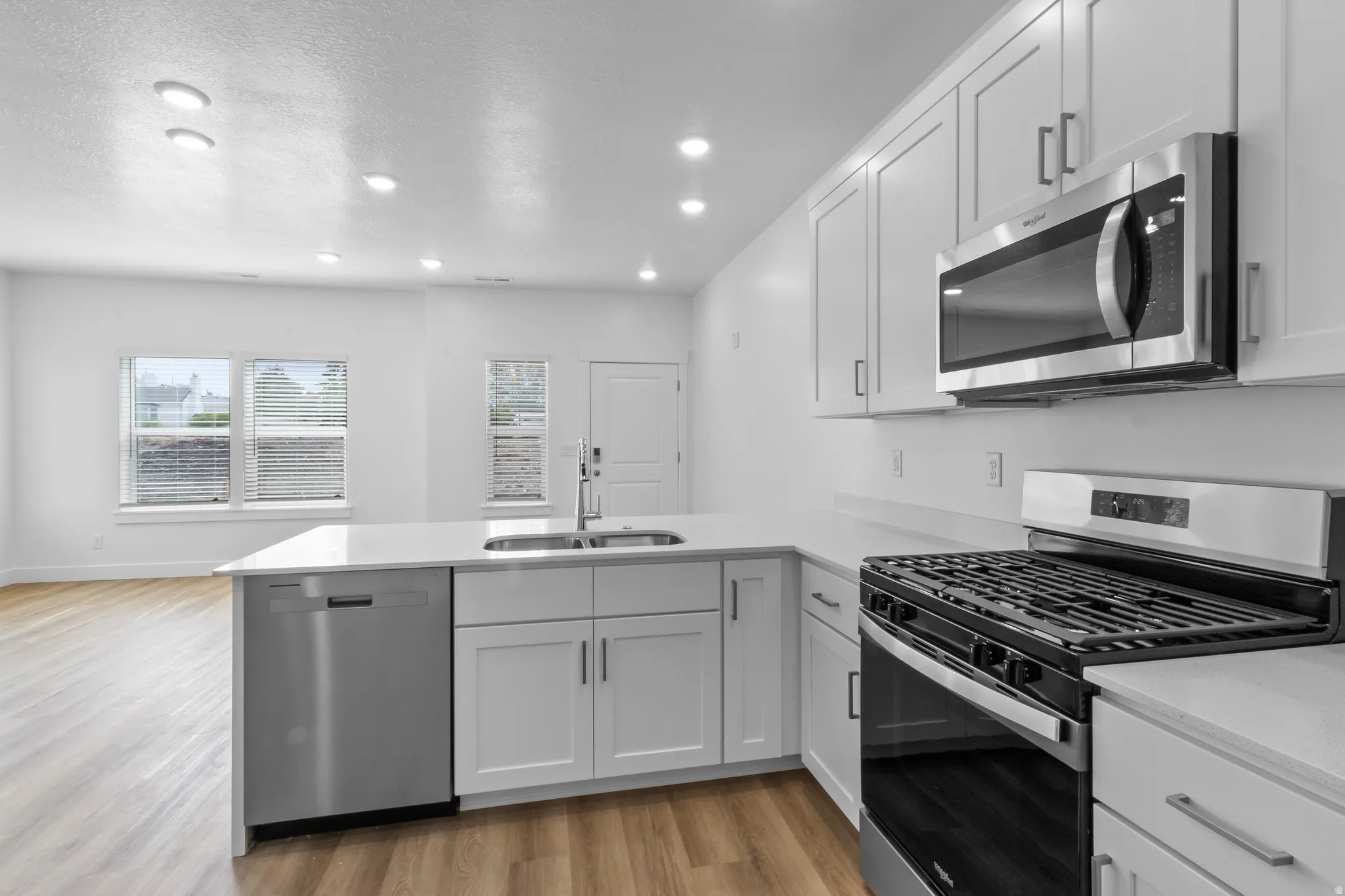 Kitchen featuring white cabinetry, stainless steel appliances, a center island with a sink, light-toned countertops, and wood-finish flooring