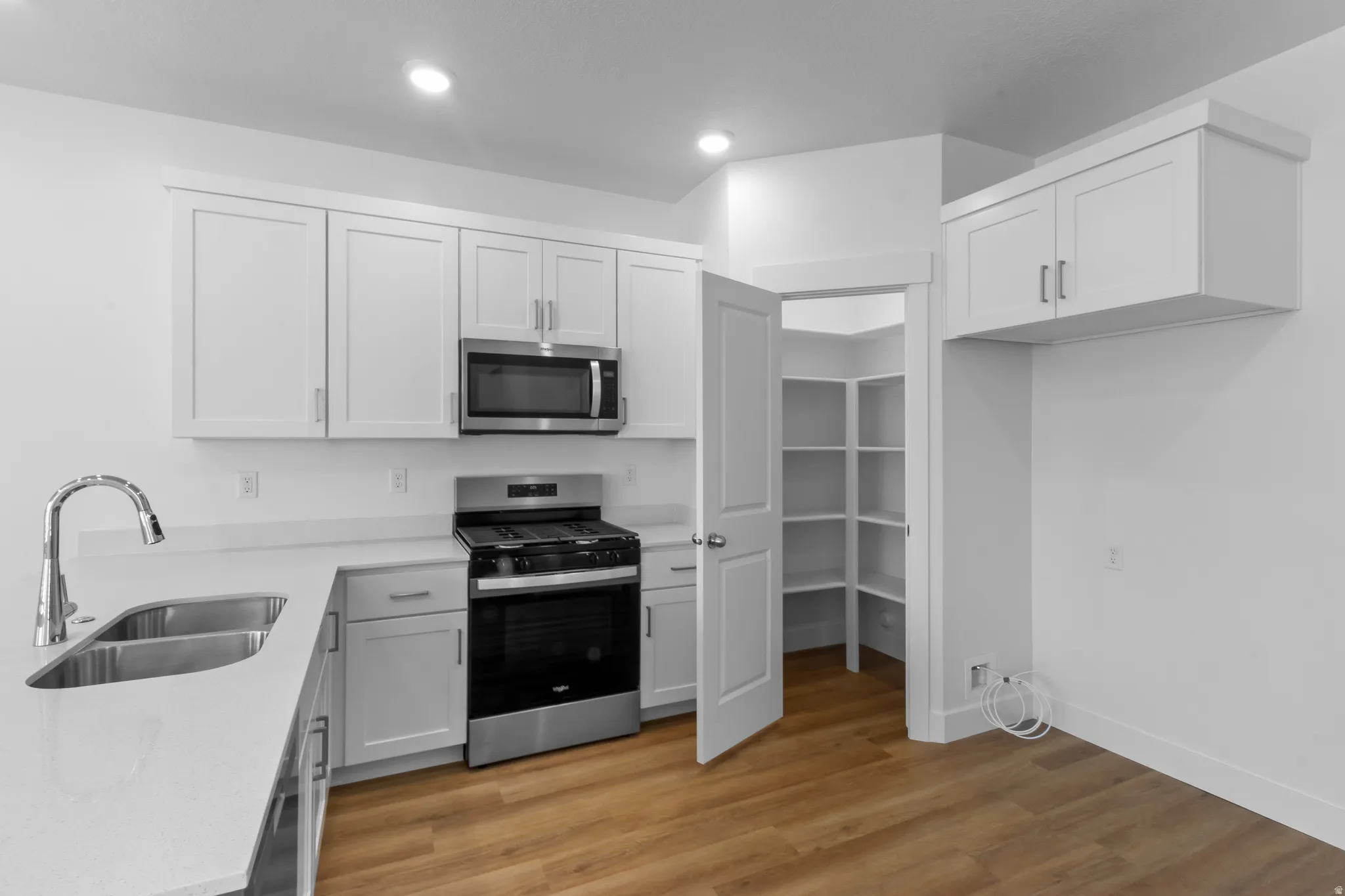 Kitchen featuring white cabinetry, stainless steel appliances, a double basin sink, and a walk-in pantry