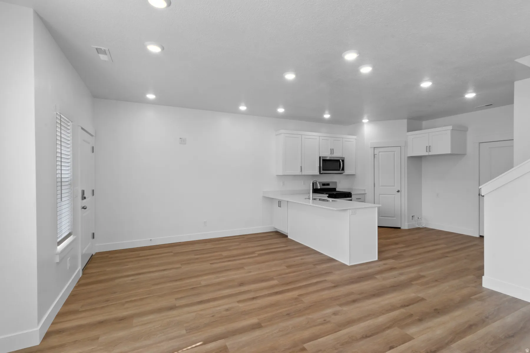 Open-concept living area featuring wood-finish flooring, recessed lighting, a white kitchen island, and stainless steel appliances