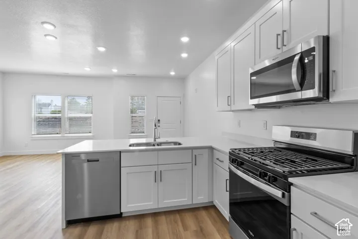 Kitchen featuring white cabinetry, stainless steel appliances, a center island with a sink, light-toned countertops, and wood-finish flooring