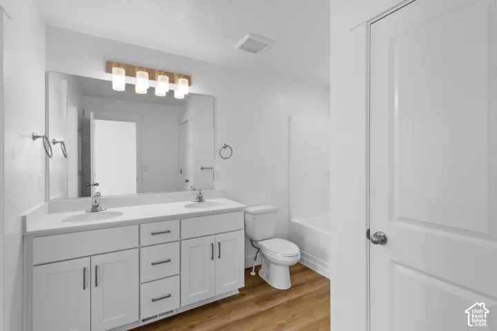 Dual sink vanity with white cabinetry, wood-finish flooring, full-width mirror, and a modern light fixture
