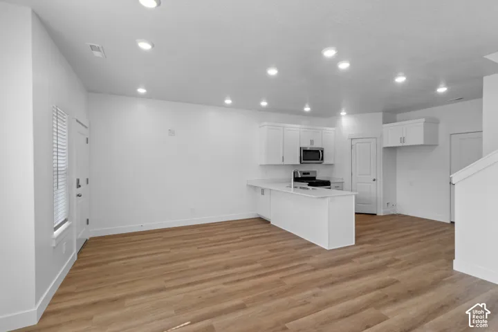 Open-concept living area featuring wood-finish flooring, recessed lighting, a white kitchen island, and stainless steel appliances