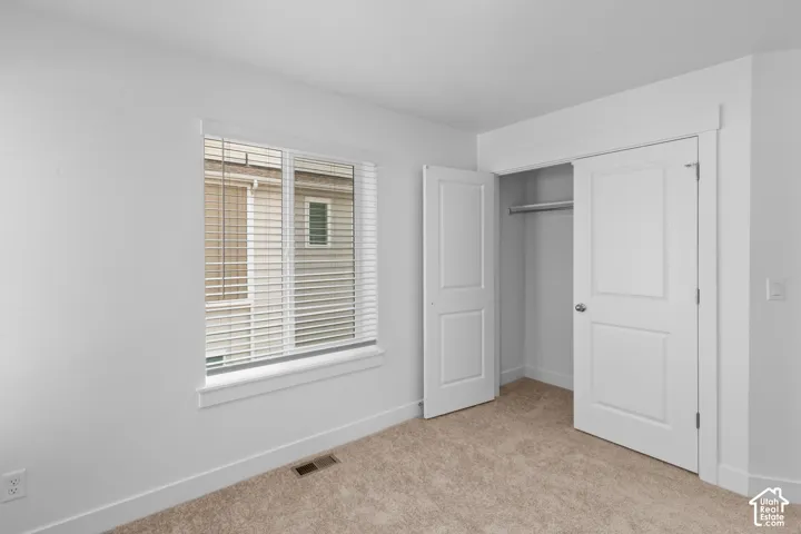 Carpeted flooring, white walls, window with blinds, and a closet with bifold doors and a hanging rod