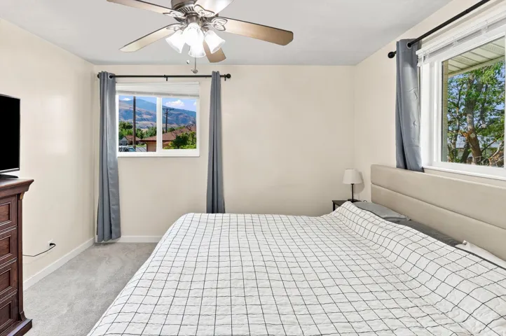 Ceiling fan with integrated lighting, two windows, wall-to-wall carpeting, and neutral wall tones