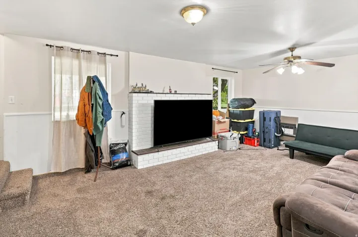 White painted brick fireplace with stone hearth, wall-mounted ceiling fan, and carpeted flooring