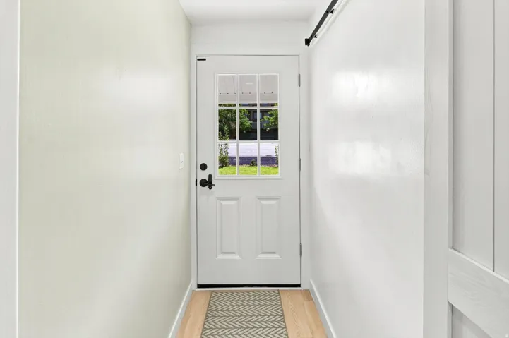 Entryway featuring a paneled door with lites, a matte black door handle, light wood-finish flooring, and a barn door track