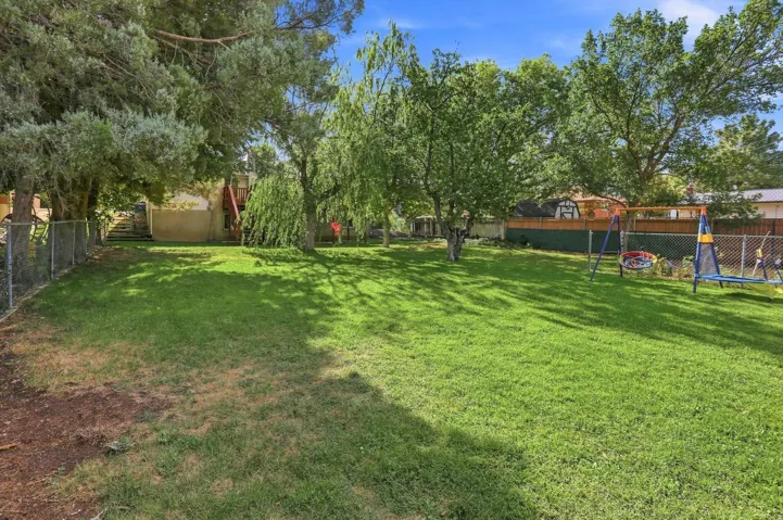 Expansive backyard featuring a lush lawn, mature trees, and chain-link fencing