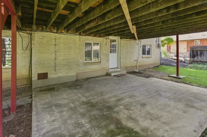 Covered concrete patio with exposed wood joists and brick wall