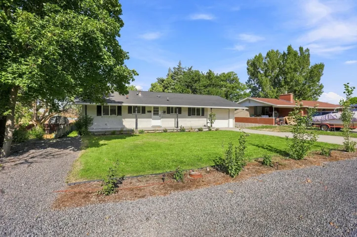 Ranch-style residence featuring a white exterior, attached two-car garage, and a gravel driveway