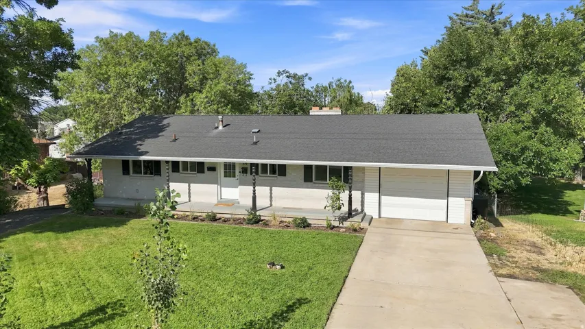 Ranch-style residence featuring a dark shingle roof, light-colored brick exterior, covered front porch with decorative columns, and an attached garage with a concrete driveway