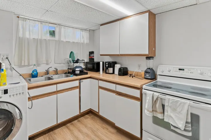 Wood-finish flooring, white cabinetry, light wood-finish countertops, stainless steel double basin sink, and a white electric range