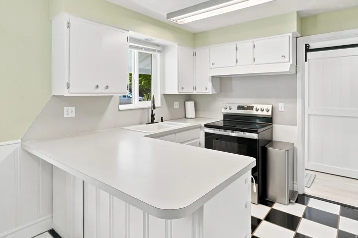 White cabinetry, U-shaped countertop, stainless steel range, white farmhouse sink with black faucet, and checkerboard floor tiling