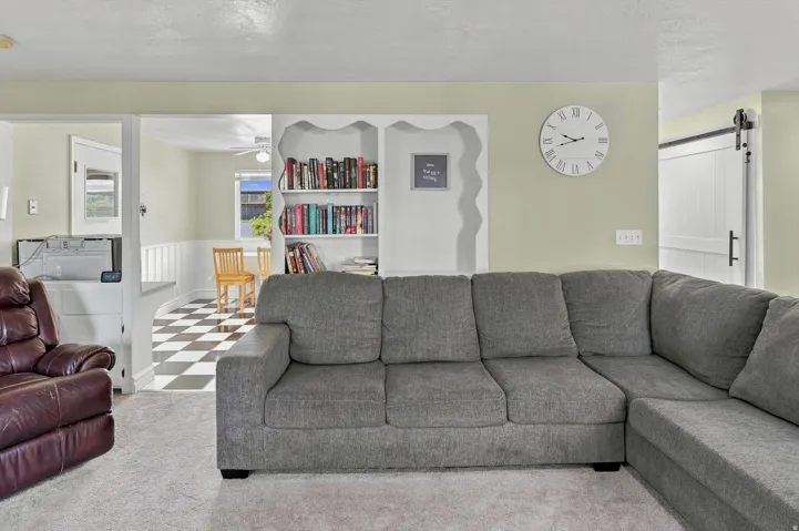 Built-in shelving unit, carpeted flooring, wood-finish sliding barn door, and checkered tile flooring in the adjacent room