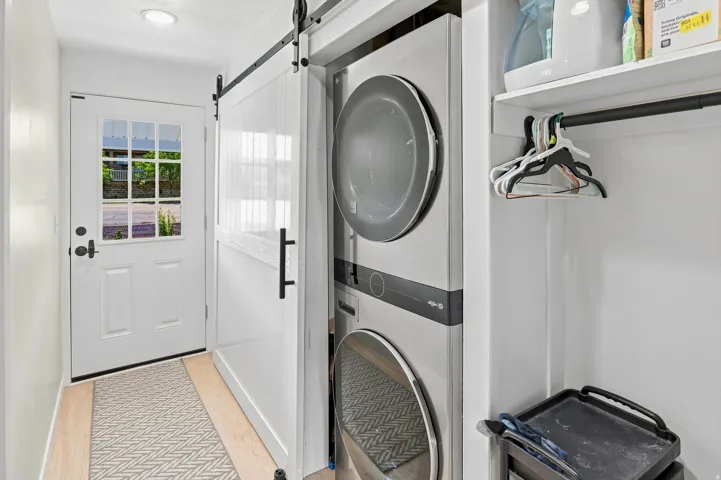 White paneled door with multiple window panes, recessed lighting, wood-finish flooring, white barn door on a black metal track, and stacked laundry appliances