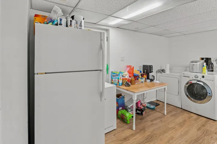 Laundry area featuring wood-finish flooring, white walls, and a drop ceiling with fluorescent lighting