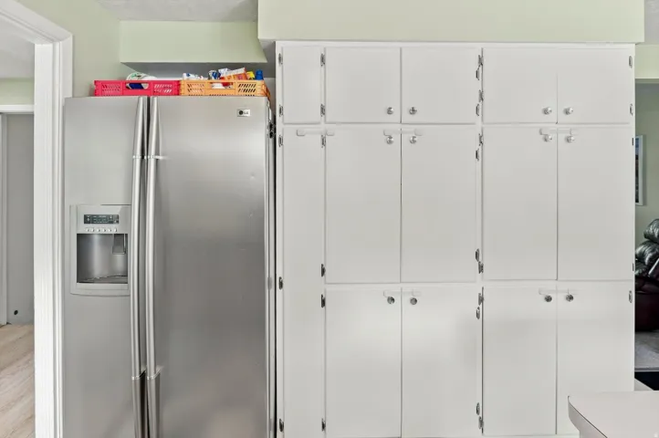 Built-in white cabinetry, stainless steel refrigerator with ice and water dispenser, and wood-finish flooring