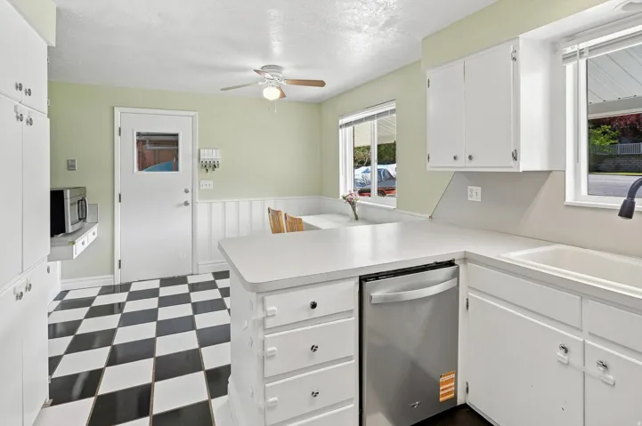 White cabinetry, black and white checkered flooring, white countertops, stainless steel dishwasher, and a ceiling fan