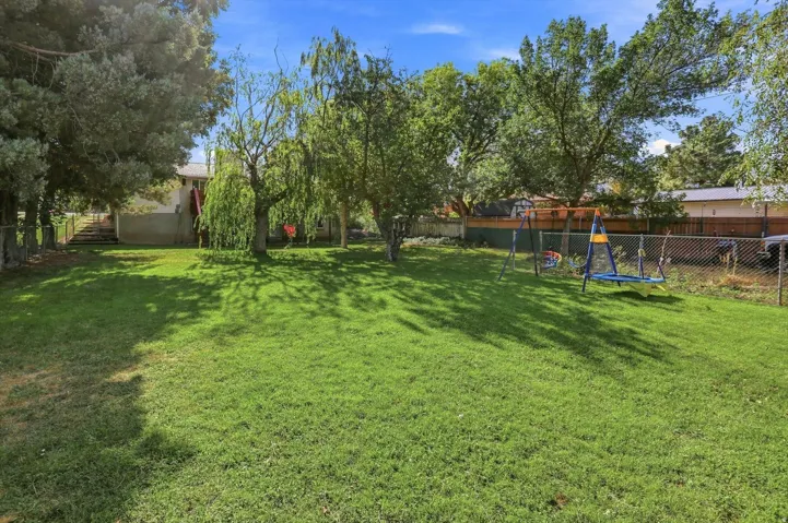 Expansive rear yard featuring a manicured lawn, mature trees, and chain-link fencing