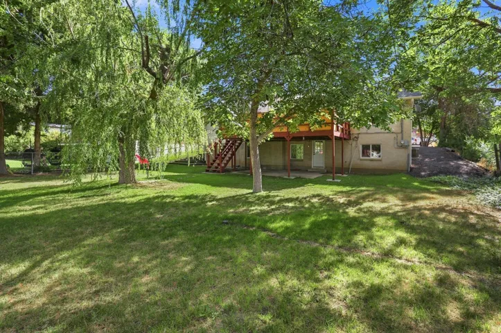Expansive rear yard featuring mature trees, a manicured lawn, and a multi-level deck with stairs
