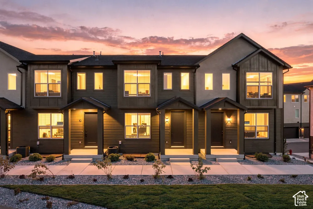 Multi-unit exterior featuring dark horizontal siding, stone-colored stucco accents, covered porch entries, multi-pane windows, and concrete walkways