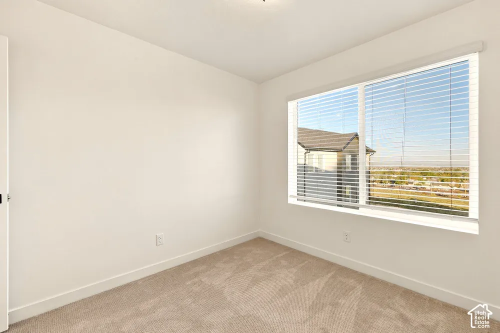 Neutral-toned wall-to-wall carpeting, expansive window with horizontal blinds, and textured neutral wall finish