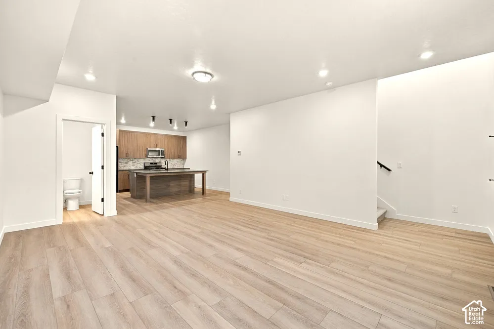 Open-concept interior featuring light wood-finish flooring, recessed lighting, a center kitchen island, and flat-panel wood cabinetry