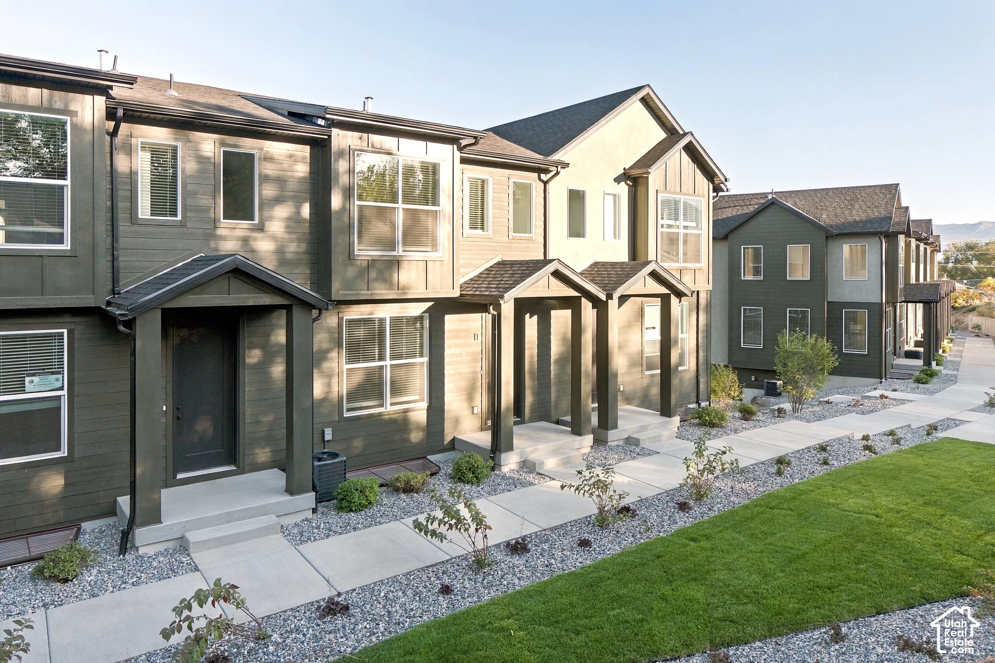 Multi-unit exterior featuring dark-toned horizontal siding, board and batten detailing, gabled entry overhangs, and concrete walkways