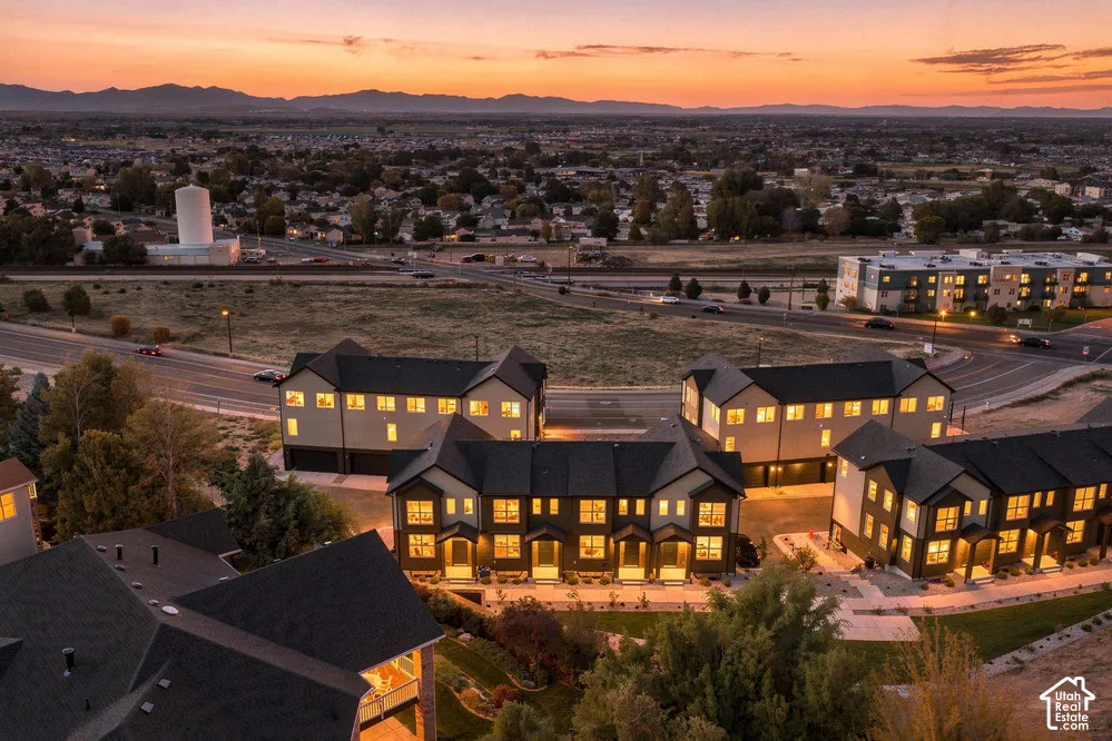 Multi-unit residential complex featuring gabled rooflines, multi-story facades, attached garage bays, and paved walkways, set against a mountain backdrop