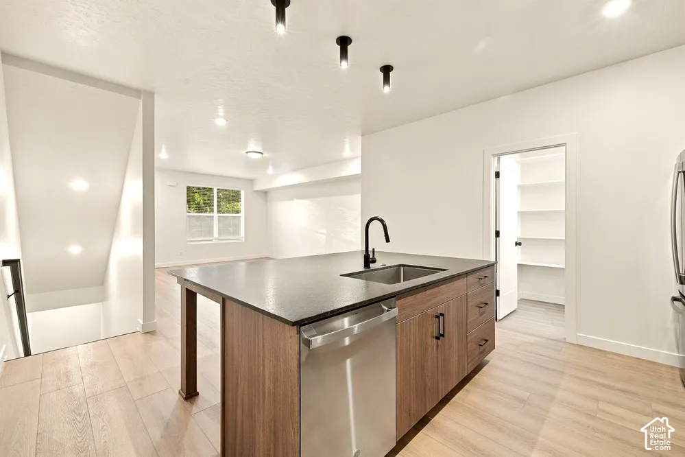 Kitchen island featuring a dark countertop, stainless steel dishwasher, and wood-finish cabinetry