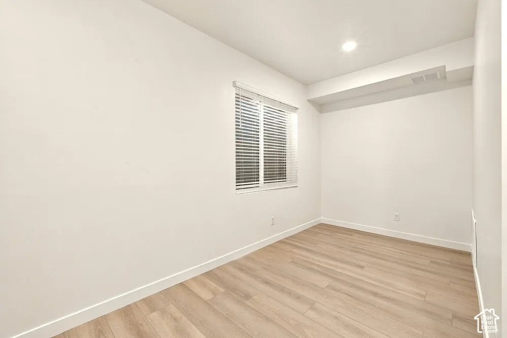 Neutral interior space featuring wood-finish flooring, crisp white walls, and a recessed ceiling light