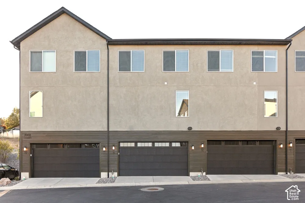 Multi-story exterior featuring a neutral stucco facade, horizontal wood-finish siding, attached garages with panelled doors, and exterior wall-mounted lighting