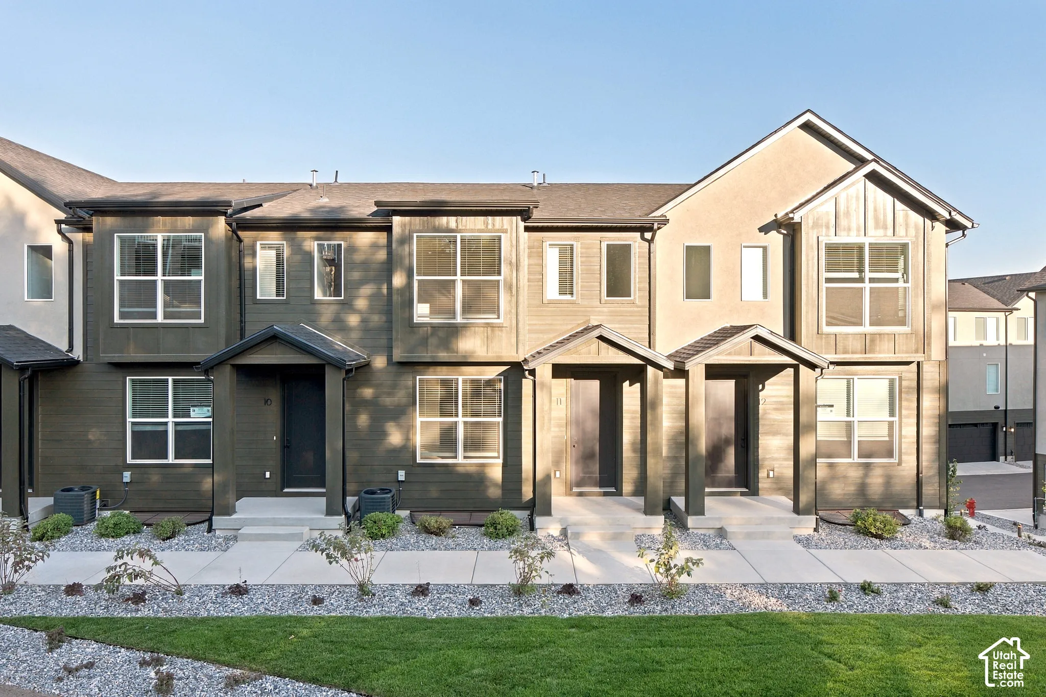 Multi-unit exterior featuring dark horizontal siding, vertical board-and-batten accents, gabled entryway covers, and concrete walkways