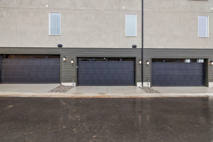 Modern exterior with stucco facade, horizontal siding, and multiple garage doors with frosted glass panels