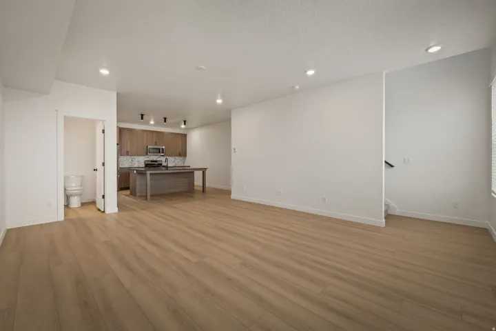 Expansive open-concept living area featuring wood-finish flooring, recessed lighting, and a kitchen with wood cabinetry, a center island, and stainless steel appliances