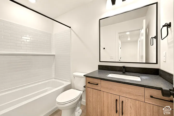 Bathroom featuring a wood-finish vanity with a dark countertop, integrated rectangular sink, matte black hardware, and a subway tile tub surround