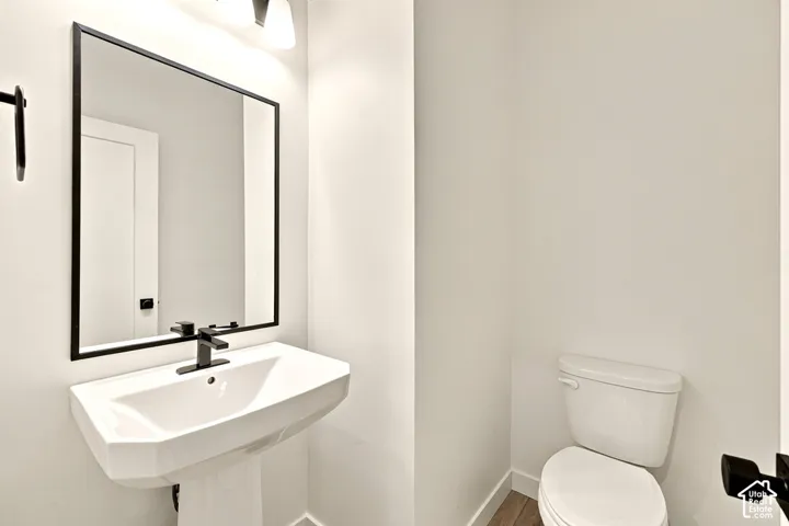Wall-mounted pedestal sink with a matte black single-handle faucet, rectangular mirror with a black frame, three-light vanity fixture, and a standard-height porcelain toilet