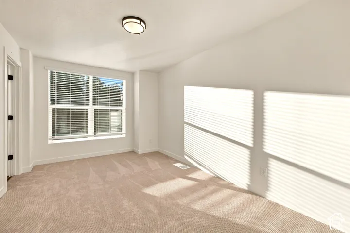 Neutral wall palette featuring carpeted flooring, large window with integrated blinds, and flush-mount ceiling lighting